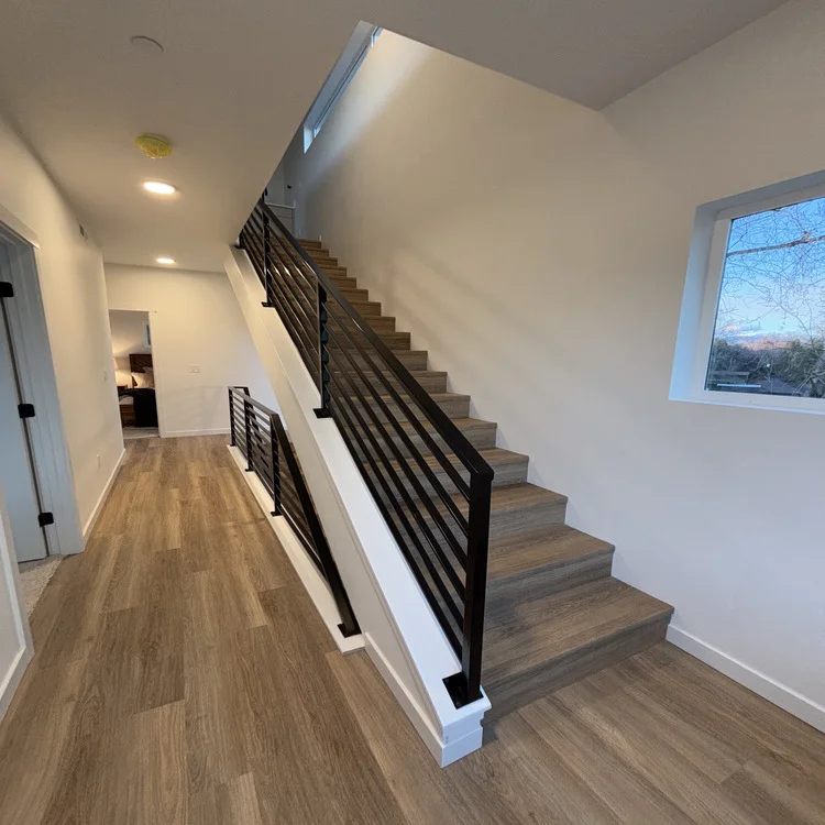 Luxury vinyl plank flooring running from a hallway up an open staircase with black metal railing