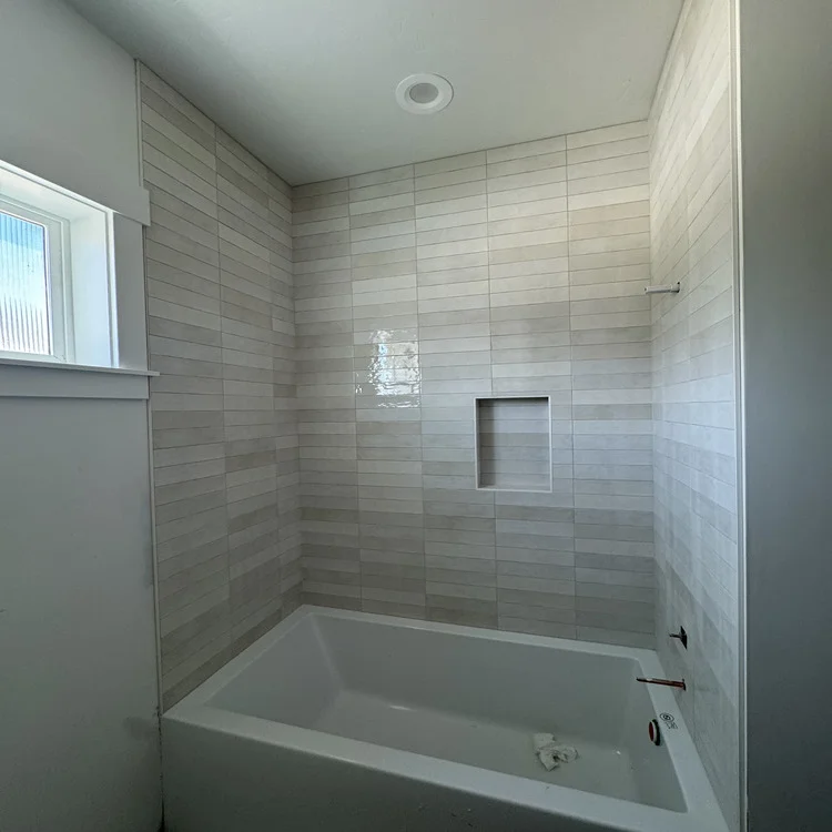 Soaking tub surrounded by plank-style porcelain wall tile with a built-in shower niche