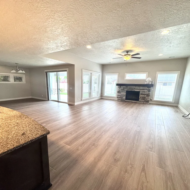 Laminate flooring in an open living room with a stone fireplace and large windows