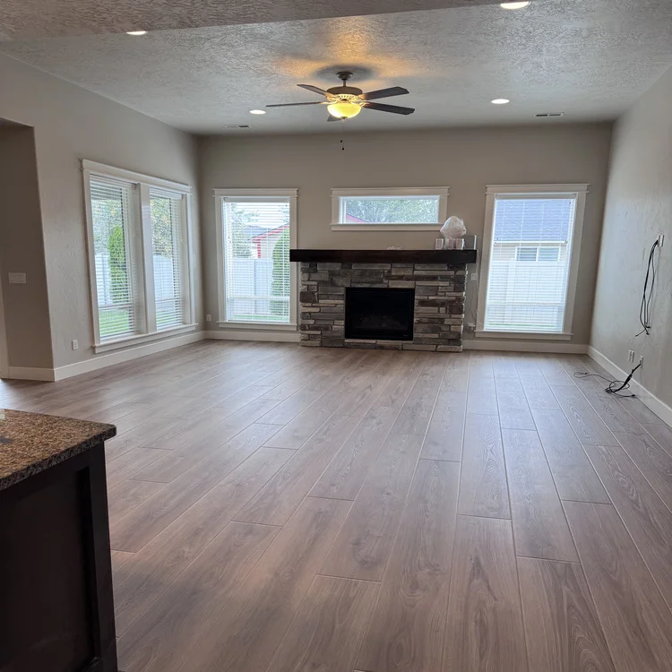 Laminate flooring in a sunlit living room with a stacked-stone fireplace surround